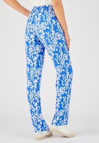 Blauwe gestreepte broek met een witte bloemenprint, voorzien van een volledig elastische tailleband en een rechte snit, gecombineerd met lichtgekleurde sneakers.