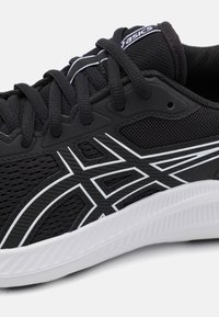 Chaussure de sport noire avec une tige en maille texturée, accents blancs et logo. Comprend un système de laçage et une semelle moulée pour une meilleure traction.