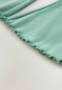 Világoszöld, bordázott szövet fodros szegéllyel; puha tapintású; strukturált kialakítású; sima felületű; a szövet egy semleges háttérre simítva van elhelyezve.