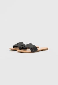 Zwarte slidesandalen met twee brede banden die in een knoopontwerp elkaar kruisen. Gemaakt van glad leer met een platte, natuurlijk gekleurde zool.