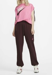 Nike pink T-shirt with logo, short sleeves, and adjustable ties; paired with burgundy jogger pants featuring logo and side stripes.