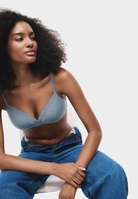 Grijze bh met kantafwerking en verstelbare bandjes, gecombineerd met blauwe high-waisted jeans, die de gladde stof en delicate details benadrukt.