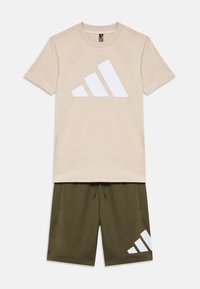 Camiseta de algodón beige con un gran logo triangular blanco, combinada con pantalones cortos verde oliva que presentan un logo a juego en el lateral.