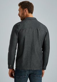 Giacca camicia grigia in misto lana con finitura testurizzata, dotata di chiusura a bottoni sui polsini e colletto, con dettaglio sul dorso.