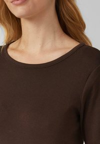 Zbliżenie szyi i górnej części klatki piersiowej osoby noszącej ciemnoszary, okrągły dekolt, długi rękaw.