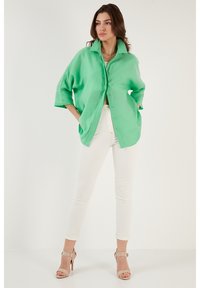 Grønt oversized skjorte med spidse krave, knaplukning foran og korte ærmer, parret med hvide skinny jeans og nude højhælede sandaler.