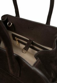 Bruine suède totebag met twee handvatten, voorzien van een binnenritsvak, beige voering en goudkleurige hardware. Logo geperst aan de binnenkant.