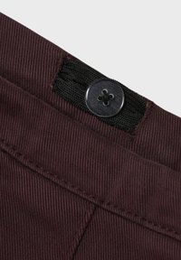 Tessuto di velluto a coste bordeaux con una superficie testurizzata, dotato di una fascia elastica nera e un bottone rotondo nero in vita.