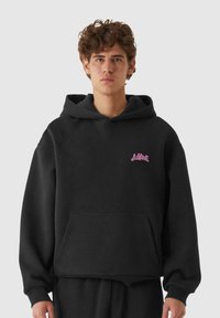 Felpa nera con cappuccio e logo rosa, tasca a marsupio, polsini a costina e vestibilità comoda. Realizzata in morbido tessuto testurizzato.