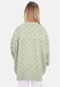 Light green oversized shirt featuring a textured fabric with white heart-patterned accents. Classic collar and drop shoulder design.