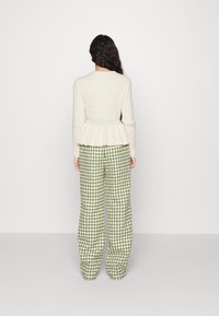 Krémový žebrovaný svetřík s volánem v pase, kombinovaný se zelenými širokými kalhotami se vzorem jehlanu. Hladká textura, přiléhavý pas a uvolněný střih.