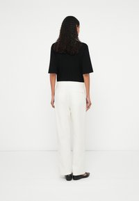 Sort ribstrikket kortærmet top og hvide bukser med vide ben, kombineret med sorte flade sko. Bukserne har en glat tekstur og lommer.