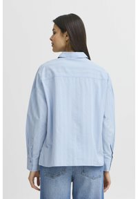 Světle modrá pruhovaná košile vyrobená z bavlny. Má límec, dlouhé rukávy s knoflíkovými manžetami a volný střih. Viditelné detaily sešívání.