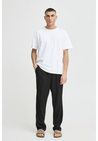 White cotton t-shirt with a classic crew neck, paired with loose-fitting black pants. Model wearing light brown sandals. Simple and casual design.