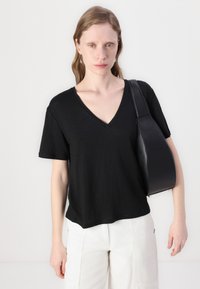 Černé tričko s vínovým výstřihem vyrobené z měkké látky, krátké rukávy. V kombinaci s černou koženou kabelkou přes rameno. Minimalistický a ležérní design.
