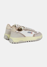 Sneakers zijn gemaakt van een combinatie van witte mesh en beige suede, met een gele middenzool en een getextureerde rubberen buitenzool, waarop branding aan de zijkant is te zien.