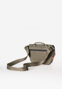 Borsa a tracolla compatta verde oliva con cinturino regolabile, tasca con zip e piccolo manico, appoggiata su una superficie bianca.