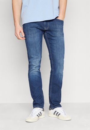 Vaqueros de mezclilla en lavado oscuro con un ajuste Slim. Presentan costuras en contraste, cinco bolsillos y una cinturilla regular. Llevados con zapatillas blancas.
