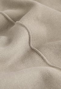 Tissu texturé brun clair avec un doux motif tissé. Le matériau présente des coutures visibles et un léger éclat satiné.