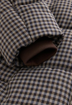 Puffer jacket with a checkered pattern in dark blue and beige, featuring a ribbed brown cuff. Textured fabric with visible stitching details.
