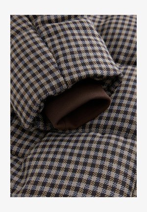 Puffy bunda s kostkovaným vzorem v tmavě modré a béžové barvě, s žebrovaným hnědým manžetou. Texturovaná látka se viditelnými švy.