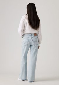 Light blue wide-leg jeans with a high waist, featuring two back pockets and a brown leather brand patch. Paired with a white, long-sleeve top.