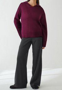 Burgundowa bluza z kapturem, z długimi rękawami i ściągaczem u dołu, zestawiona z ciemnoszarymi spodniami o szerokich nogawkach i czarnymi płaskimi butami.