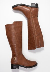 Bottes en cuir marron hautes avec zip latéral, talon bas, bout rond et sangle décorative avec anneau en métal sur fond blanc.