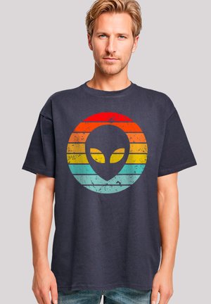 Dark navy cotton T-shirt featuring a distressed, multicolored alien graphic within a circular design, with red, orange, yellow, and teal stripes.