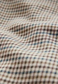 Geweven stof met een houndstoothpatroon in bruin, crème en blauwe tinten. De textuur is glad met een subtiele glans.