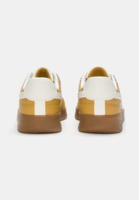 Żółto-białe trampki z fakturowaną cholewką ze skóry i podeszwą z gumy naturalnej, charakteryzujące się prostym designem i kontrastującymi białymi akcentami.