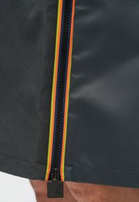 Gros plan sur un tissu gris présentant une fermeture éclair avec des accents multicolores : des rayures orange, jaune et bleu marine le long de la fermeture éclair.