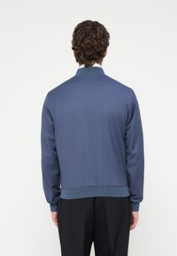 Μπλε υφασ�μάτινο μπουφάν με ριμπ πλαινό λαιμό και μανσέτες, με εφαρμοστή σχεδίαση και ελαστική μέση, από πίσω όψη.