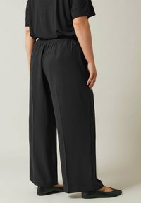 Zwarte wijde broek gemaakt van zachte stof met een elastische tailleband en zijzakken, biedt een losse fit en een gladde textuur.