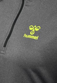 Czarny szary pół-zamek z miękkiego materiału, zdobiony żółtym logo "hummel" oraz czarnym zamkiem błyskawicznym biegnącym pionowo.