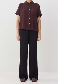 Camicia bordeaux a maniche corte con colletto, bottoni e taschino sul petto, abbinata a pantaloni larghi neri e ballerine nere con texture.