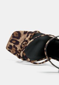 Sandale à talons à imprimé léopard avec un bout carré, une tige en tissu doux et des fines sangles noires. La semelle est plate et texturée.