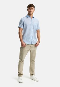 Lichtblauw kortemouw overhemd met een textuurpatroon en een borstzak, gecombineerd met beige broek en witte sneakers.