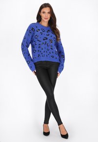 Zila pūkaina džemperis ar melnām sekunšu leopardu plankumiem, garām piedurknēm, apaļa dekoltē līnija. Saskaņots ar augsto vidukli melnām legingām un melnām kurpēm ar augstiem papēžiem.