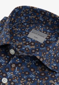 Sininen paita kukkakuviolla, jossa vaaleanruskeita ja kermaisia yksityiskohtia; siinä on kapea kaulus ja tagi nimeltä "DAN JOHN SLIM." Napit ovat valkoiset.