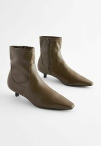 Bottines en cuir marron avec un bout pointu, un petit talon et une fermeture éclair sur le côté. Texture lisse avec des détails de couture visibles.