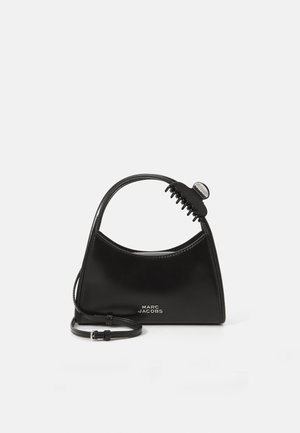 Črna torbica Marc Jacobs z ukrivljenim ročajem in pritrjenim črnim lasnim klipom na belem ozadju.