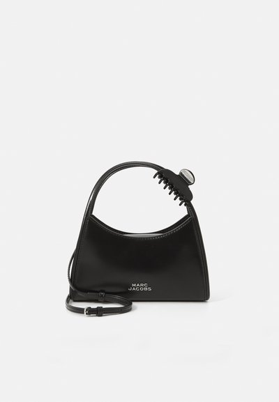 Μαύρη τσάντα Marc Jacobs με καμπύλη λαβή και προσαρτημένο μαύρο κλιπ για μαλλιά σε λευκό φόντο.