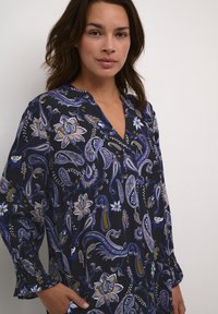 Cămașă cu model marin care combină designuri florale și paisley, având un guler în V, mâneci lungi și manșete bufante pentru o croială relaxată.