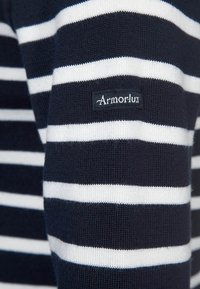 Maglione a righe blu navy e bianche con texture in maglia; presenta un piccolo etichetta nera con "ArmorLux" cucita sul lato.