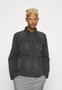 Sort denimjakke med knaplukning foran, to brystlommer og to sidelommer; har krave og en afslappet pasform.