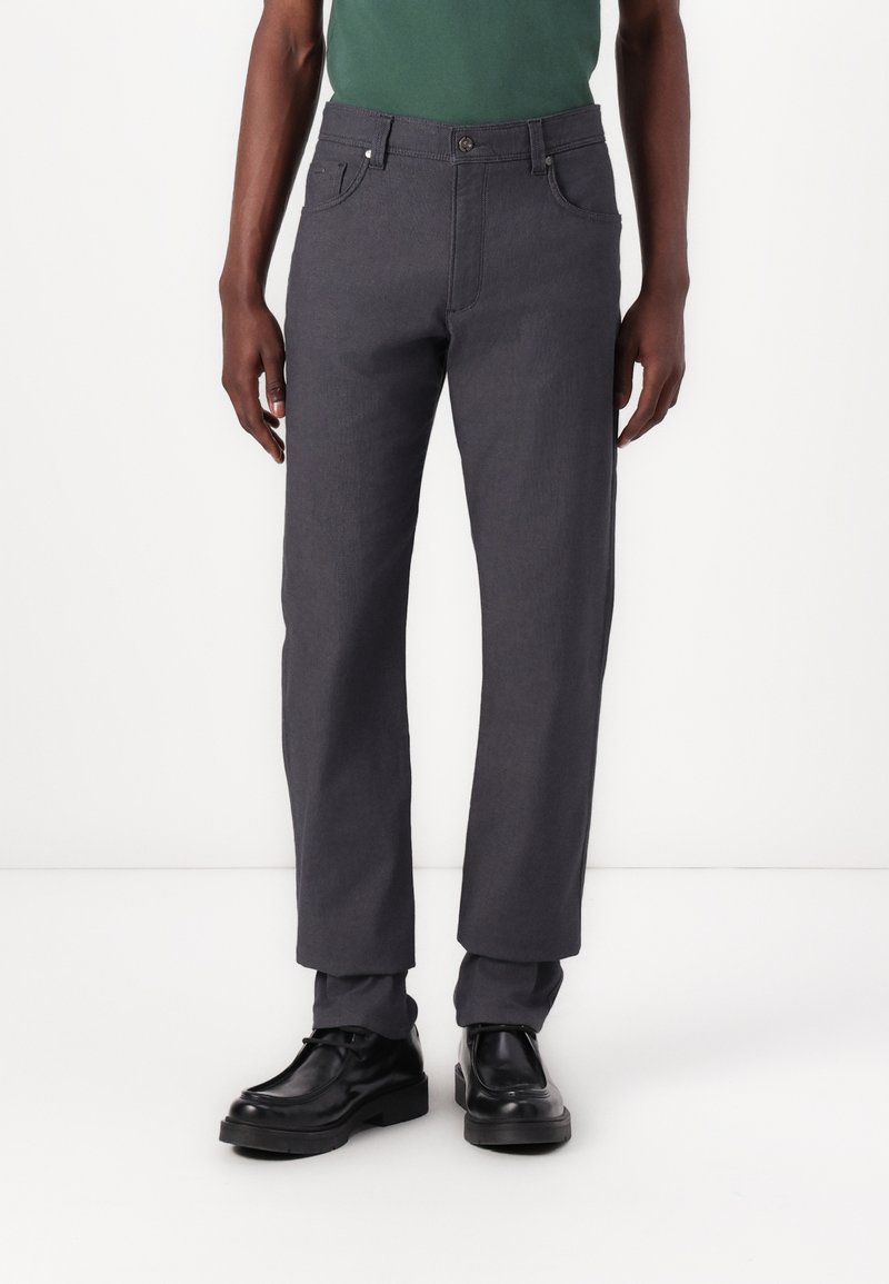Grijze, rechte broek gemaakt van een textuurstof, met zijzakken en een knoopsluiting. Gedragen met zwarte schoenen.