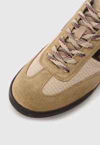 Light brown suede sneaker with textured beige mesh panels, flat laces in beige and burgundy, and a black rubber outsole.