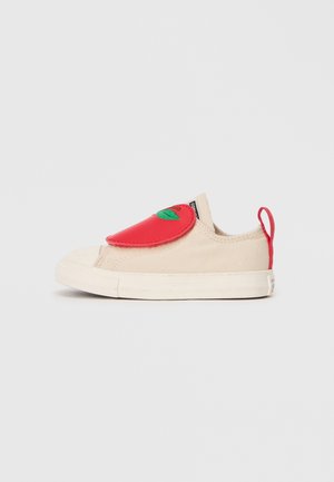 Baskets en toile beige avec un rabat en caoutchouc rouge arborant un motif de feuille verte. Capuchon texturé à l'avant et une languette rouge à l'arrière pour un enfilage facile.