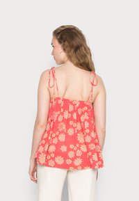 Top floral em coral com alças finas, apresentando um design franzido e padrões de margaridas amarelas pálidas. O detalhe nas costas inclui laços. Material suave.